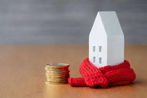 Home energy costs concept with house model wrapped in scarf and coins